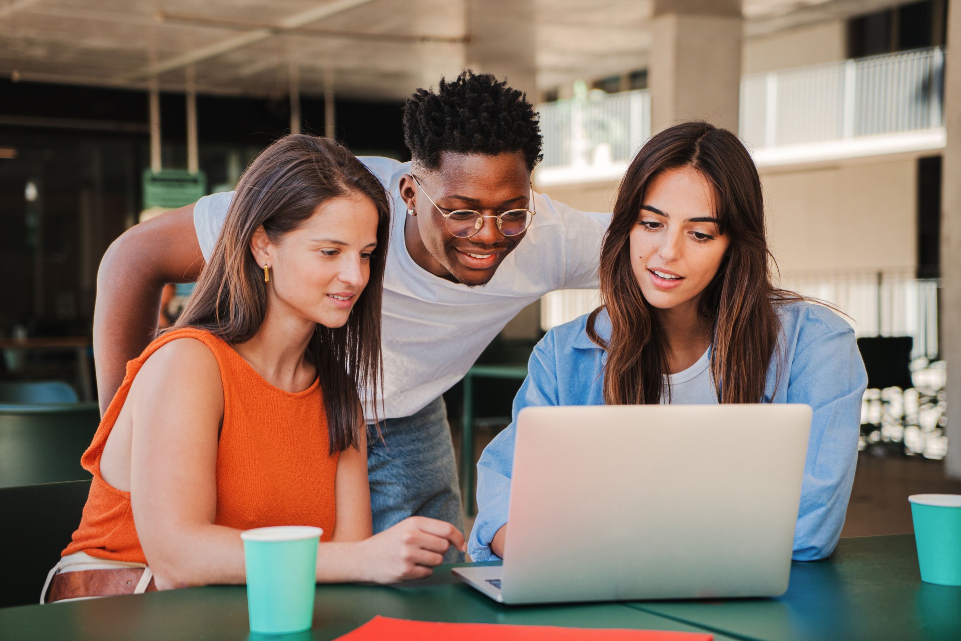 Group of multiracial happy teenage students using laptop, working on university assignment homework project in college library. Meeting of diverse young people looking information on computer